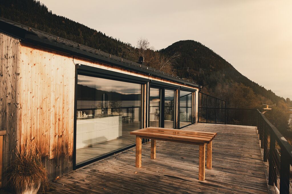 The glass wall and deck of the timber house, with the forested mountain behind