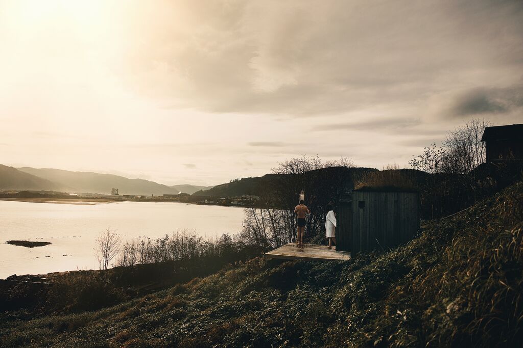 Two guests by the sauna on the fjord shore in soft golden light