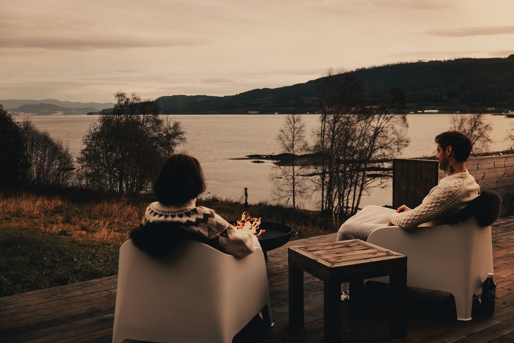 Two guests in wool sweaters on the terrace, looking out over the fjord