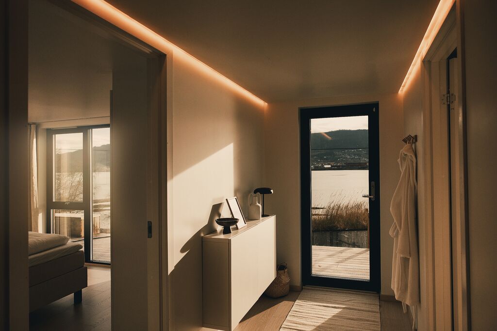Hallway with warm ceiling light and a robe by the glass door out to the deck and the fjord