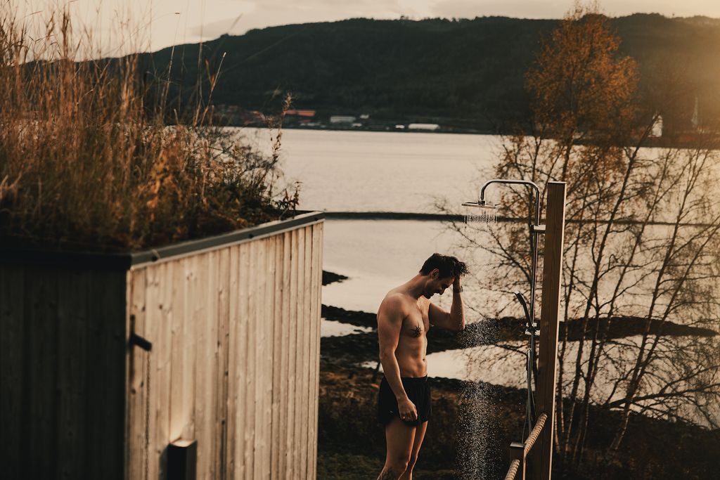 A guest under the outdoor cold shower on the deck, the fjord behind