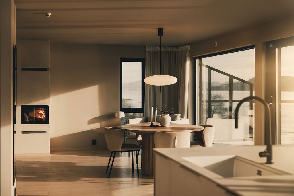 Sunlit dining table by the fireplace, with the fjord through the windows