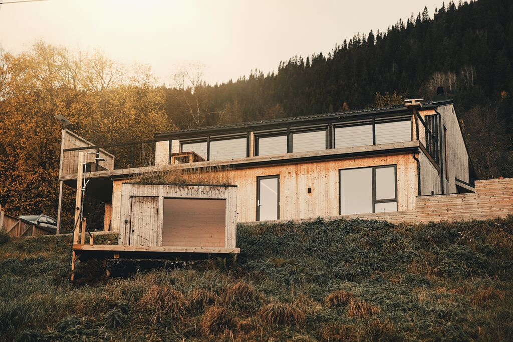 The timber house and sauna on the hillside, with autumn trees and forest behind
