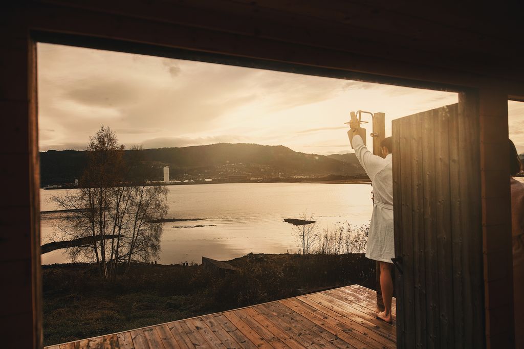 View from the sauna door over the fjord at sunset, a guest in a white robe on the deck